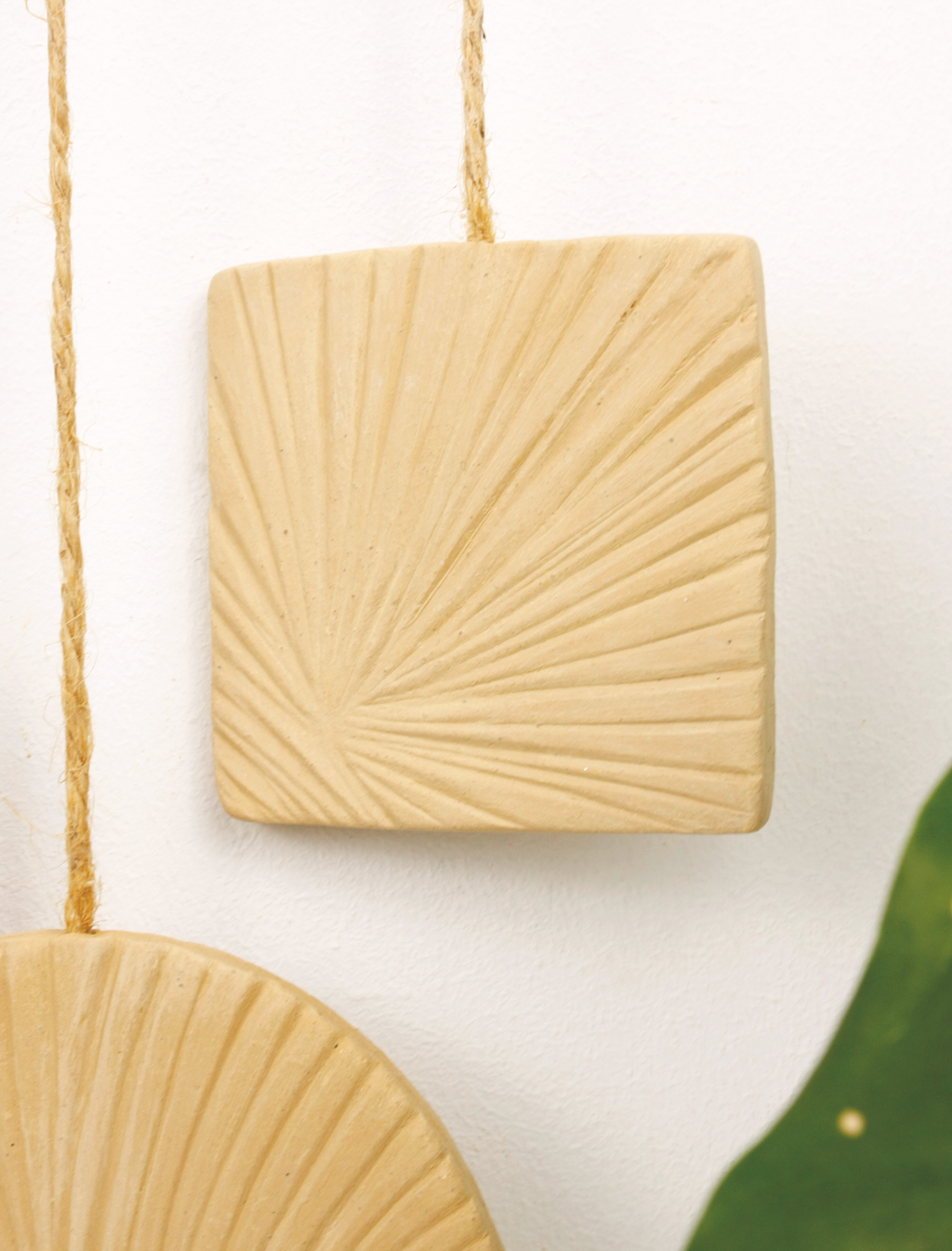 Beige ceramic wall hanging with sunburst pattern on a white background