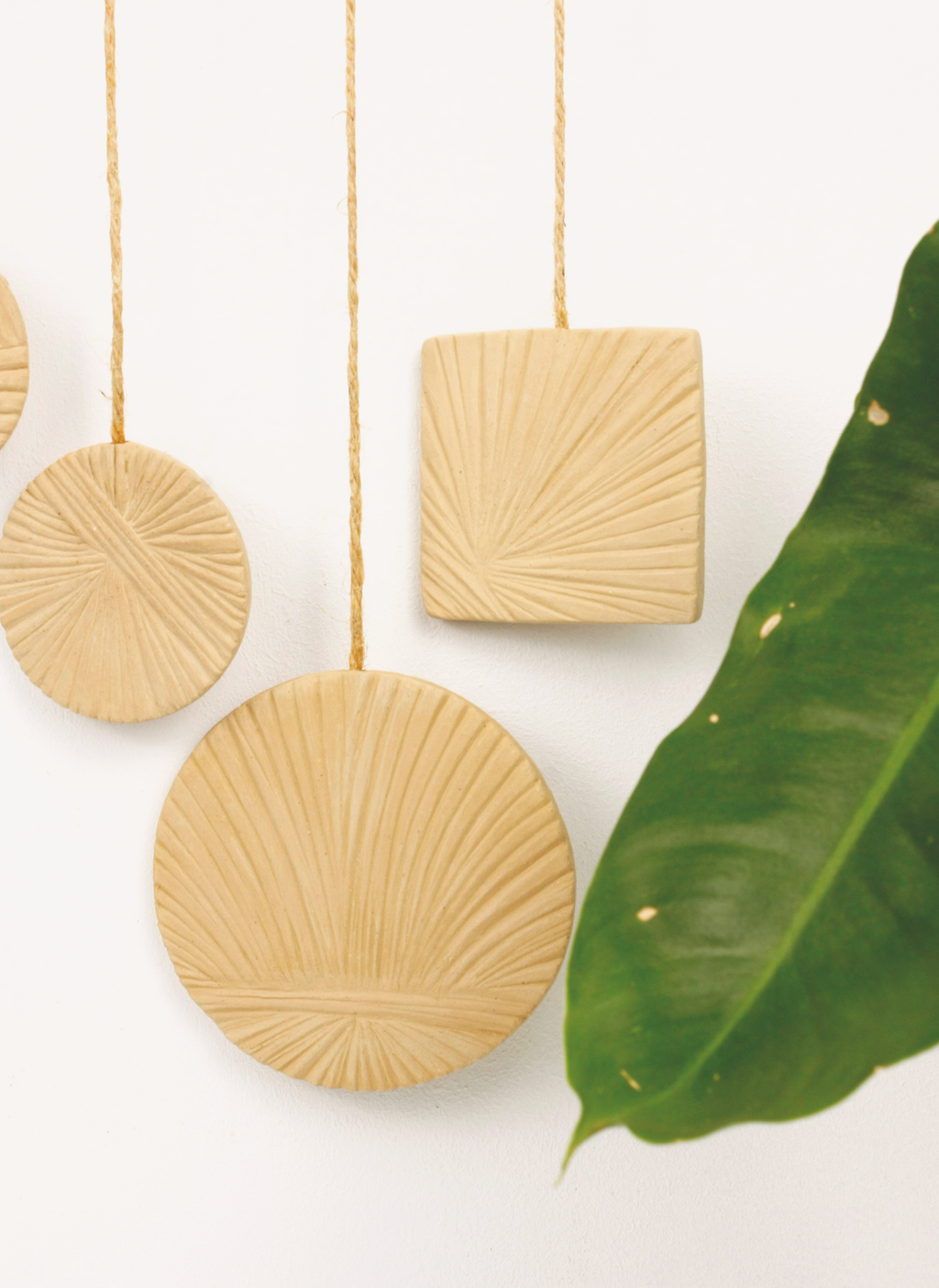 Decorative beige ceramic wall hangings with a green leaf on a white background